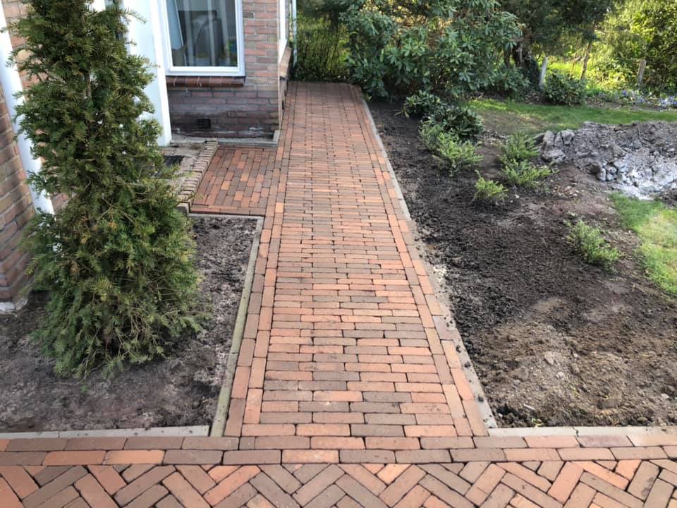 Tuinpad in rode klinkers langs het huis, met een haag ernaast