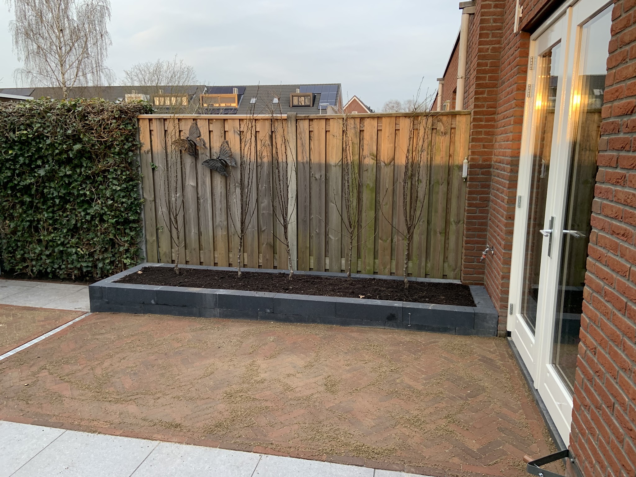 Achtertuin met een nieuwe zwarte plantenbak langs de schutting en een zandbed voor de bestrating