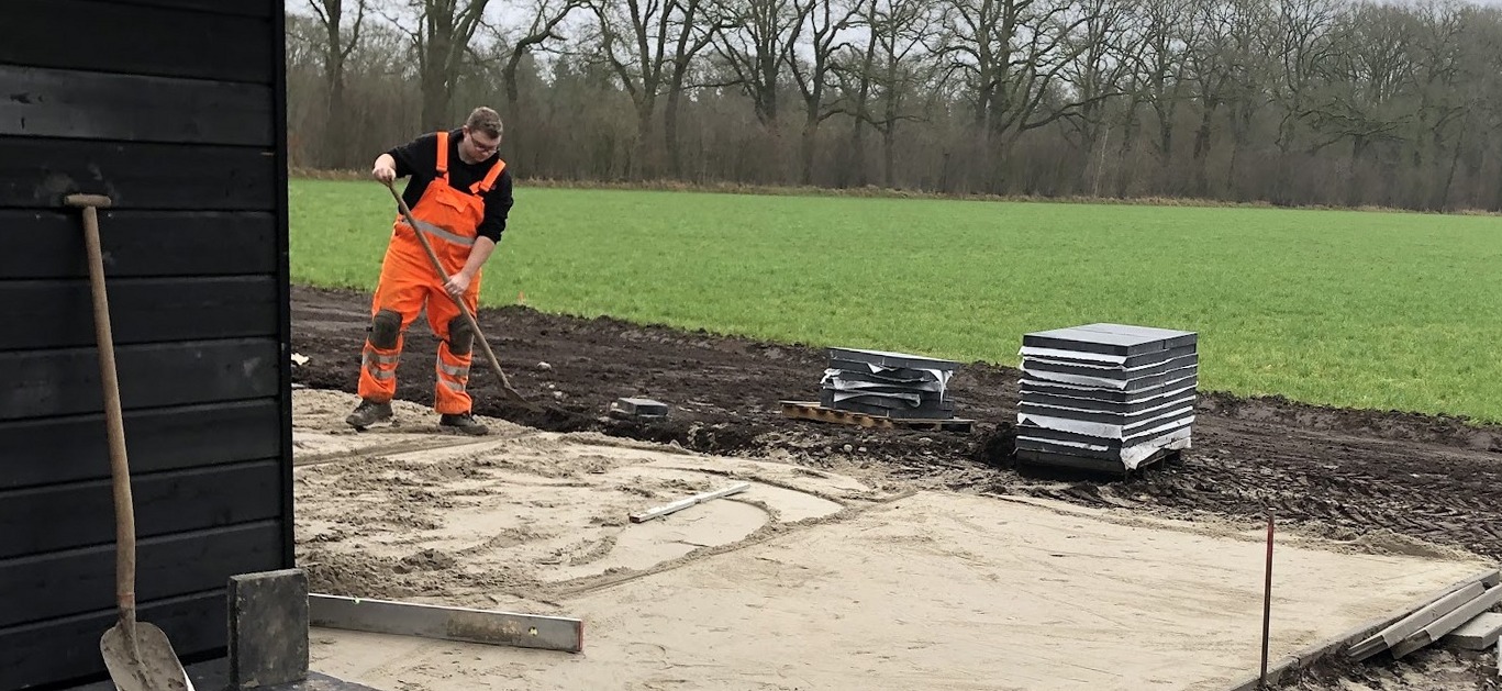 Een stratenmaker harkt het zandbed vlak naast een nieuwbouwwoning met zwarte gevelbekleding